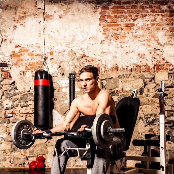 Uomo che si allena con bilanciere su panca palestra Gorilla Sports, muro in mattoni a vista.