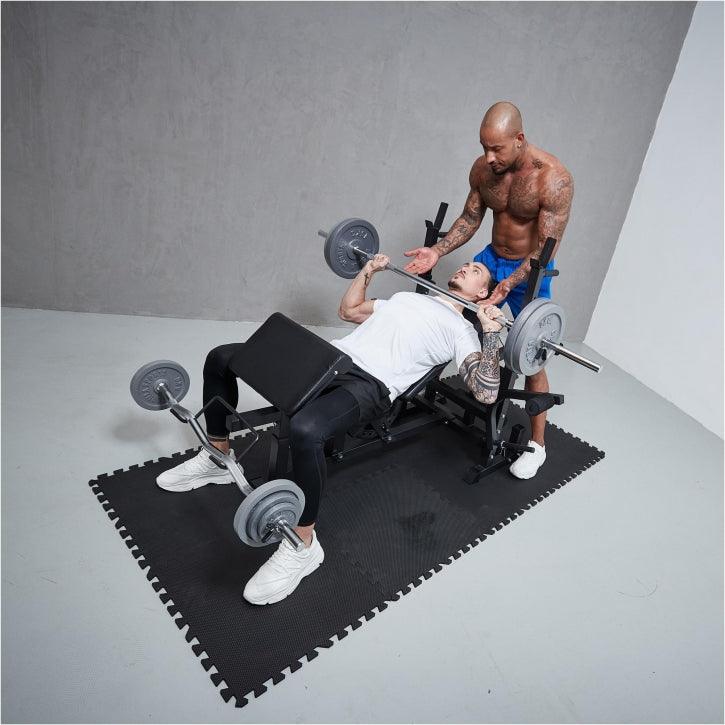 Allenamento bodybuilding Gorilla Sports: uomo in panca con bilanciere, istruttore assiste