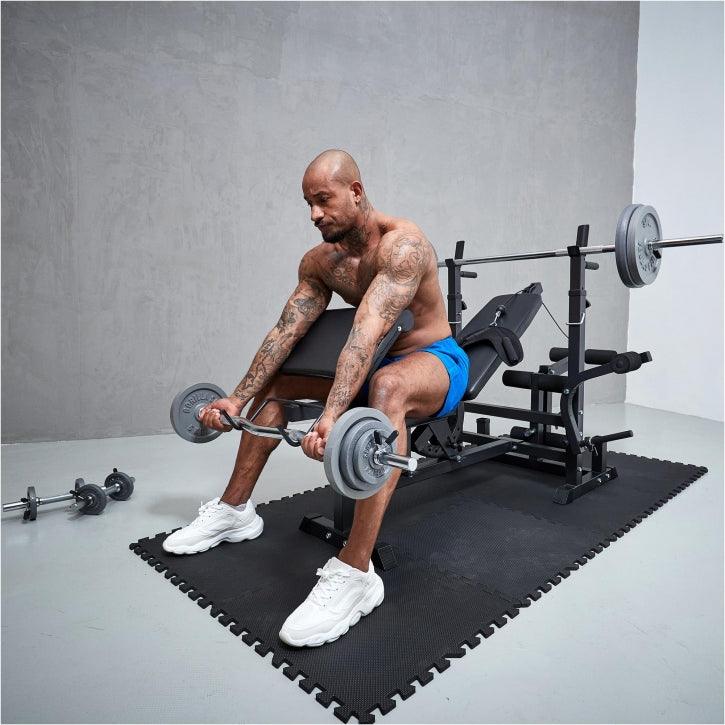 Uomo che si allena con bilanciere su panca fitness Gorilla Sports, palestra domestica