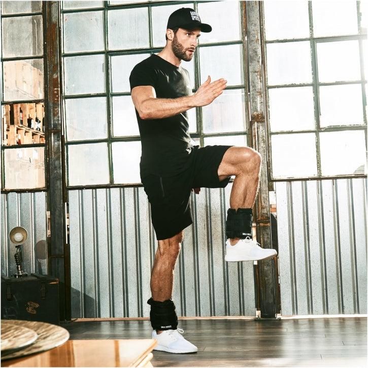 Uomo che fa esercizio fitness con pesi alle caviglie Gorilla Sports in palestra luminosa